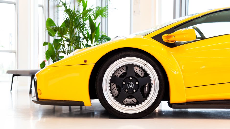 A detailed shot of a yellow supercar's wheel and body, indoors with bright lighting.